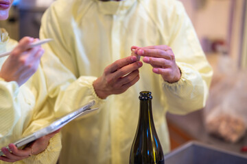 Quality control technician closely examines a sample in a beverage bottling facility while a...