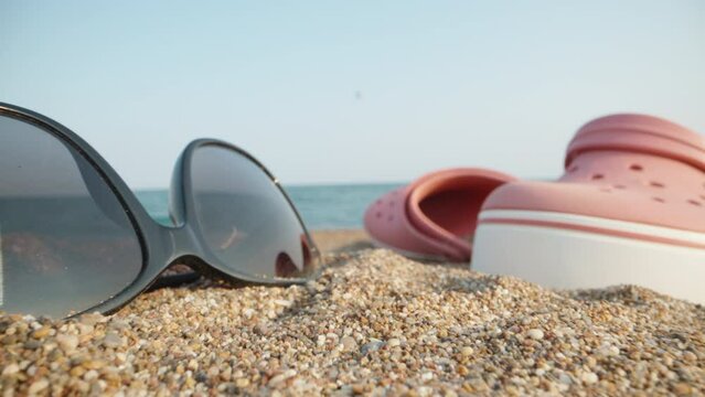 Things on the beach by the sea. Through pink flip flops and sunglasses and a red apple. Dolly slider extreme close-up.