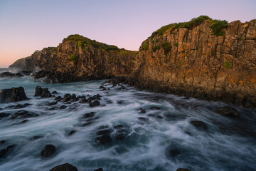 Wave water flowing around the rocky coastline cliff.