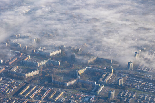 aerial high altitude image of town, earth covered in layer of fog or mist in early morning soft sunshine light. Clouds cover houses and apartments in town or city