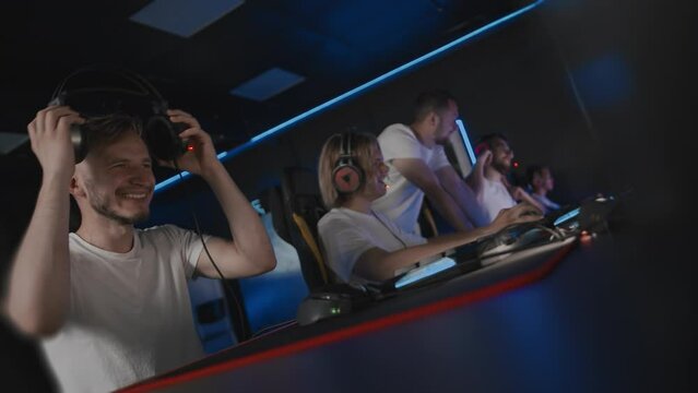 Coach and team wins round game in E-sport cyber tournament. Gamers play video game on PC at computer club. Tactics strategy trainer. 5 Caucasian players in headset. Happy emotions. High-five gesture