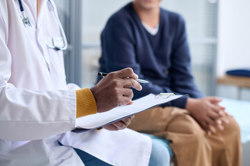Side view closeup of Middle Eastern doctor holding clipboard while consulting child in clinic copy...