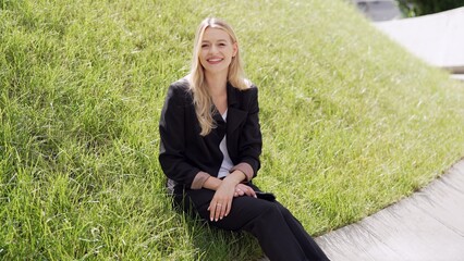 Smiling Woman in Black Suit Sitting on Green Grass