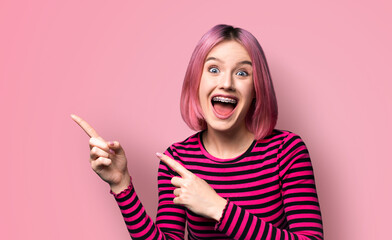 Excited very happy pink haired woman in braces, open mouth, wear red striped jumper sweater advertise peeking pointing area for sales slogan text, isolated background. Dental care ad advertisement. - obrazy, fototapety, plakaty