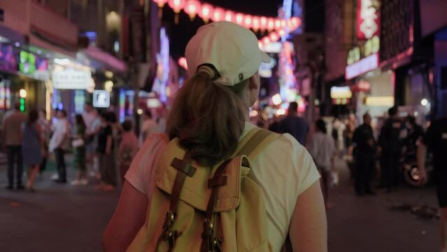 Woman tourist walking along night street among crowd of people.