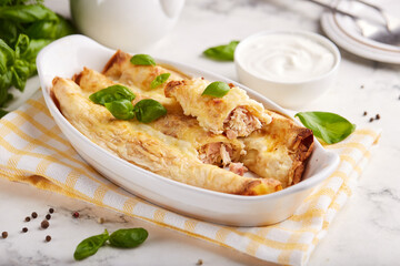 Crepes rolls stuffed with chicken meat, ham and cheese, baked with bechamel sauce and cheese. 