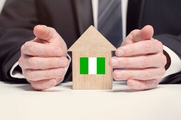 Businessman hand holding wooden home model with Nigerian flag. insurance and property concepts