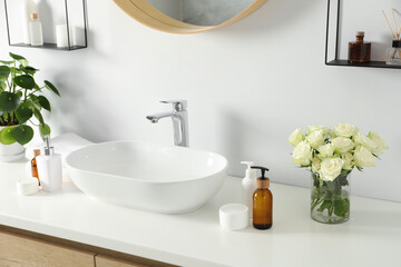 Beautiful roses, houseplant and bath accessories near sink in bathroom