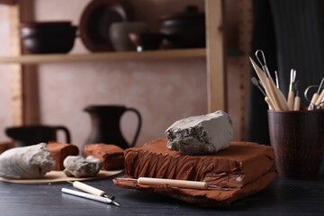 Clay and set of modeling tools on dark gray wooden table in workshop