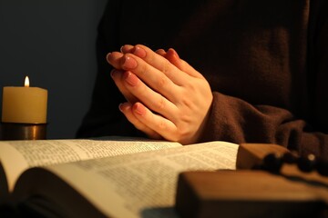 Obraz premium Woman praying at table with burning candle and Bible, closeup