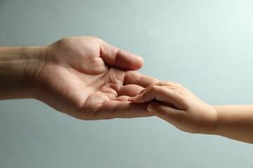 Father and child holding hands on light blue background, closeup