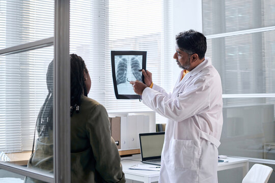 Side view portrait of senior doctor pointing at chest x ray while consulting patient in clinic copy space