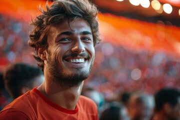handsome smiling man with perfect teeth looking at camera, football fan wearing t-shirt during football match. Blurred crowd in the background. Concept of healthy skin care, aesthetics - obrazy, fototapety, plakaty