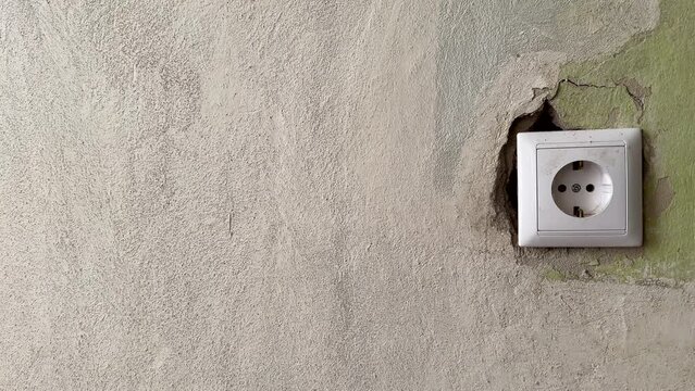 Broken electrical socket hanging on the wall. Plug socket hanging off the wall in room. Damaged electrical plug. Socket fell out of wall and hangs on wires. Repair in the house of old sockets