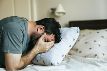 man sobbing into a pillow on his bed