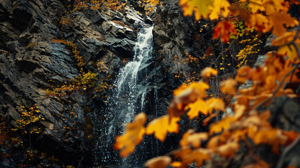 A narrow waterfall streaming down a vertical rock face surrounded by autumn-colored foliage.