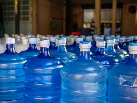 Many blue gallons and white gallon of drinking water are lined up in a drinking water production plant.