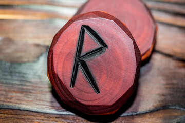 Rune Raido red color carved from wood on a wooden background - Elder Futhark