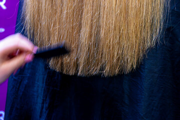 A hairdresser straightens the long hair of a fair-haired girl, trimming the ends.