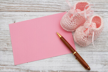 Pink baby booties with pink greeting card with pen on weathered wood