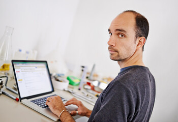 Man, laptop and equipment in workshop, brewery and portrait with scroll, research and development. Person, computer and typing at factory on web for alcohol, craft beer and tools on desk in warehouse