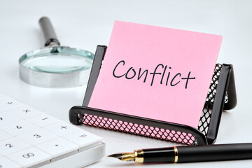 Conflict word on a pink sticker with office supplies on a white background