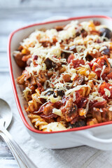 Baked fusilli pasta with cherry tomatoes, olives and mozzarella cheese. Bright wooden background. Close up.	