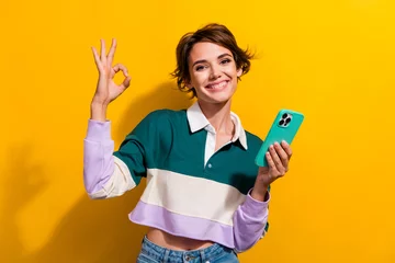 Deurstickers Photo of pretty nice young girl hold cellphone show okey symbol wear shirt isolated on yellow color background © deagreez