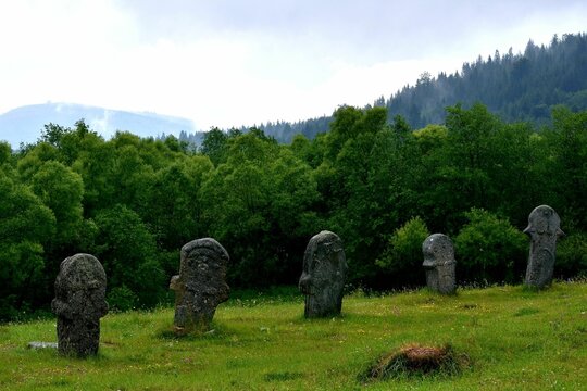 Row of medieval tombstone stecak stones in a lush green field