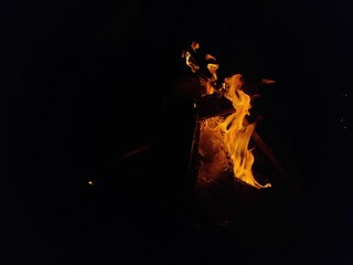 Campfire burning brightly in the night sky, with orange and yellow flames consuming the wood