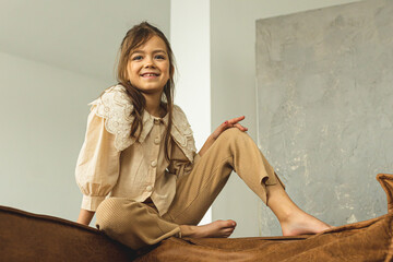 A cute and happy little girl is sitting on the sofa. Teenage girl. The girl is playing and enjoying life