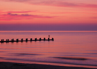 Scenic view of a pier on a tranquil sea at pink sunset
