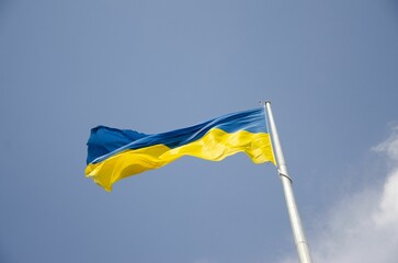 Low-angle shot of the flag of Ukraine waving in the breeze against a blue sky.