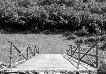 Old wooden bridge, standing out against a lush green field in the background - obrazy, fototapety, plakaty