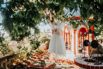 Elegant white infant dress for the baptism ceremony hangs from a tree in an outdoor setting