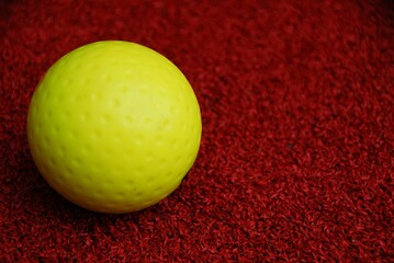 Isolated close-up of a bright yellow ball resting on a flat, red surface.