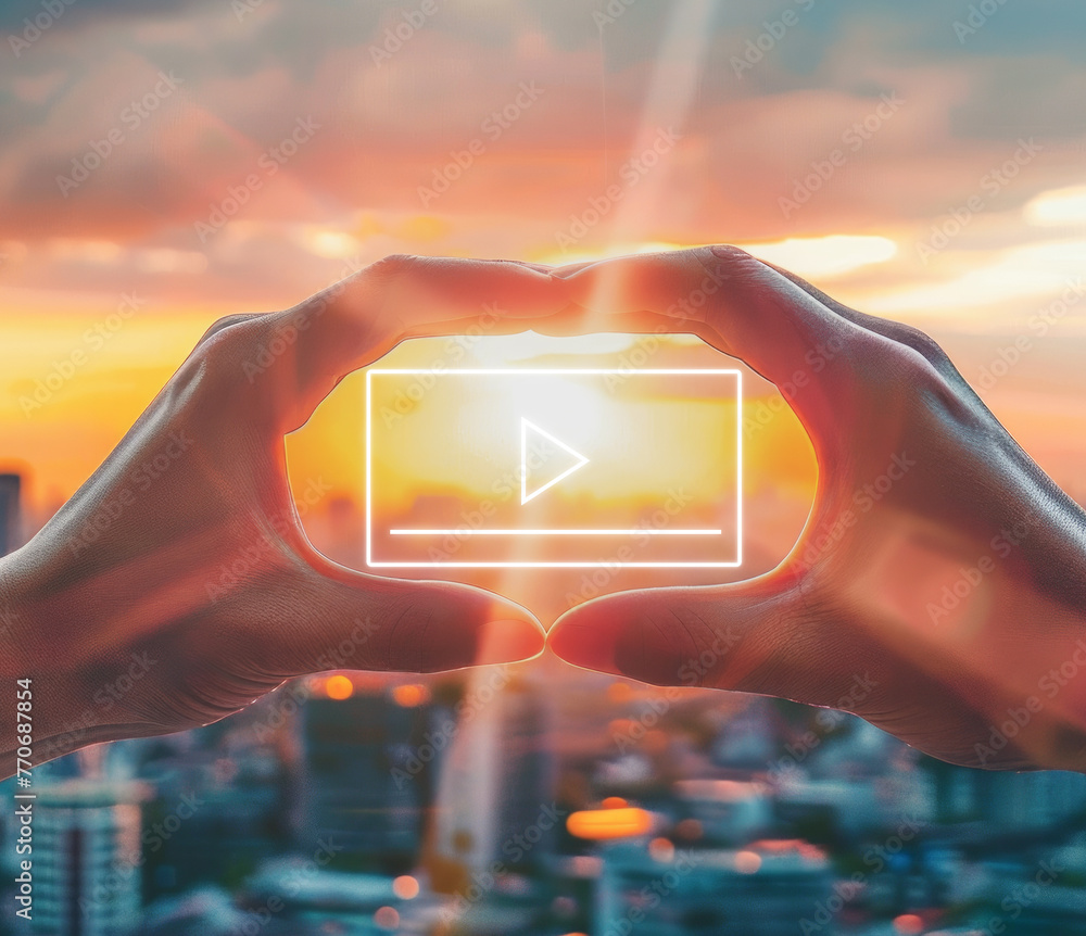 Poster hands framing a digital play button against a city sunset, symbolizing media or video concepts, gene