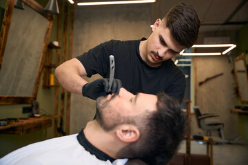 Bearded man getting beard haircut by barber at barbershop