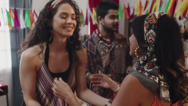 Medium slowmo shot of young beautiful Mexican woman hugging female friend or sister while greeting or saying goodbye after home party, while husbands are chatting in background
