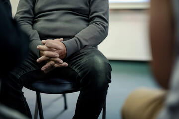 Close-up view of a person sitting on a chair in a waiting area, with others in the background. Healthcare facility reception area, feeling anxiety and anticipation for their medical appointments