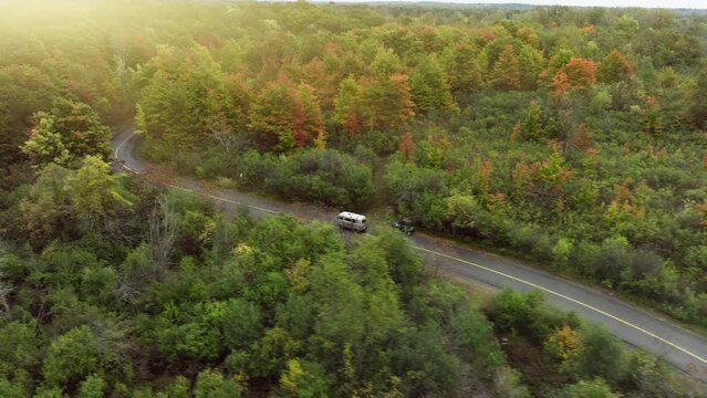 Drone footage of camper van driving on a narrow road through an autumn woods along the lake
