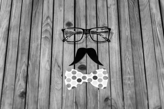 Prop made of glasses, paper black mustache, colored bow tie on a wooden background for a carnival. Photo of a gentleman man's face, concept, copy space.