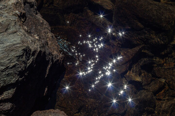Twinkling lights in the dark water of a stream. A rock, crystal clear water.