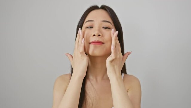 A serene asian woman touches her face gently against a white background, evoking skincare beauty.