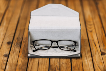 Stylish, fashionable glasses with clear lenses for good vision with black frames lie in a leather case on a wooden background. Close-up photography, business concept, work accessories. - obrazy, fototapety, plakaty