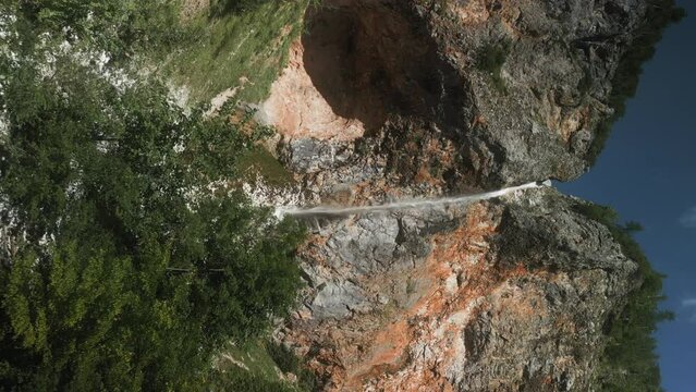 Drone shot of adult man standing on wooden footbridge taking pictures to Rinka Waterfall, Slovenia