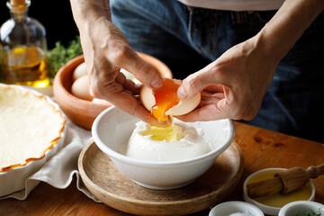 Hands while cracking an egg into the cheese mixture while preparing the pastry, close-up