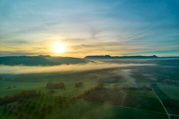 Majestic view of a foggy valley landscape with  sun setting over the green fields