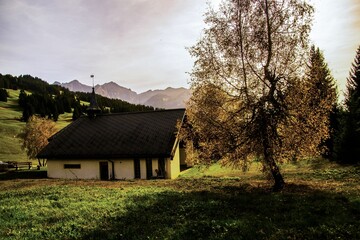 Single-story rural house situated on a lush green hill overlooking a majestic mountain range - obrazy, fototapety, plakaty