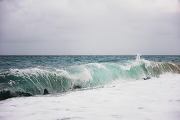 Large wave in the ocean crashing onto the shoreline, creating a white foam